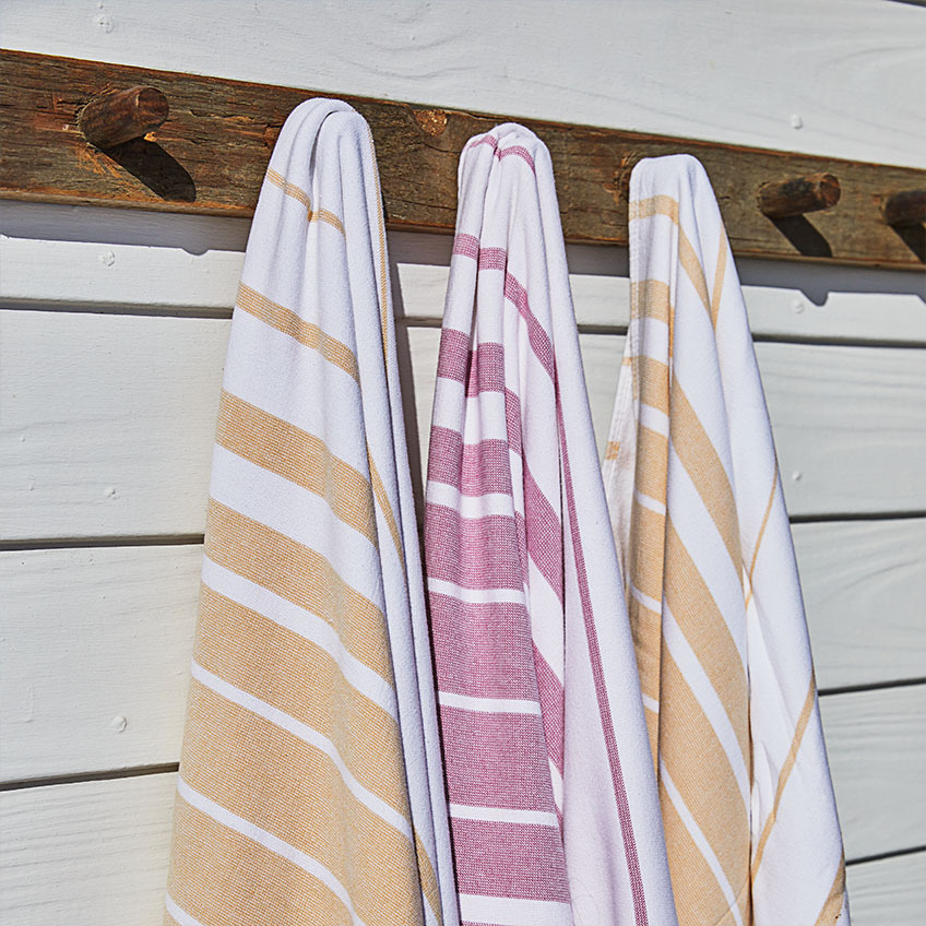 BACKA beach towel with striped patterns in white, orange, and pink Striped beach towels in white, orange, and pink fuchsia hanging on wooden wall